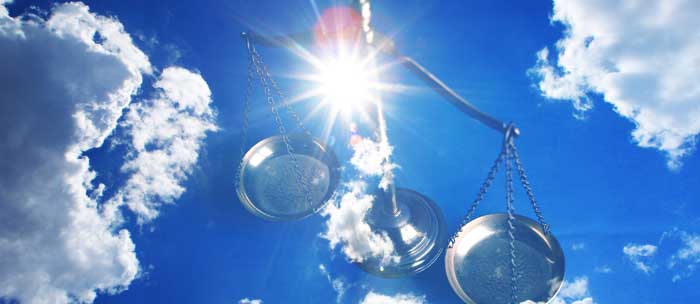 An image of a balance scale is superimposed over an image of a bright sun in cloudy sky.